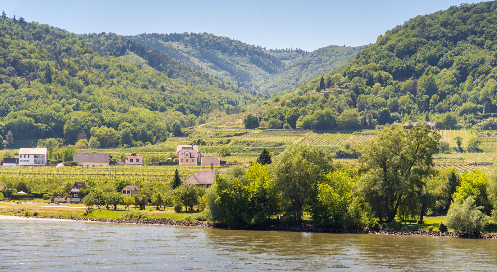 Kuće se nalaze pored reke u podnožju brdovitih vinograda prekrivenih bujnom zelenom šumom pod vedrim nebom