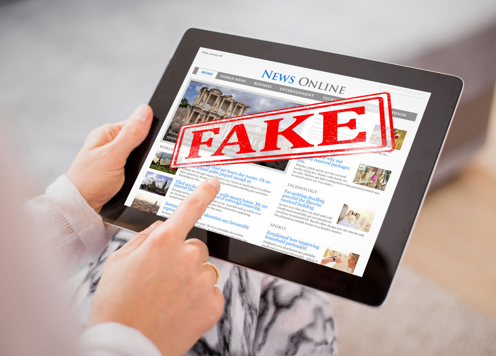 Ženske ruke drže tablet na čijem ekranu piše vesti i crveni pečat sa natpisom lažno