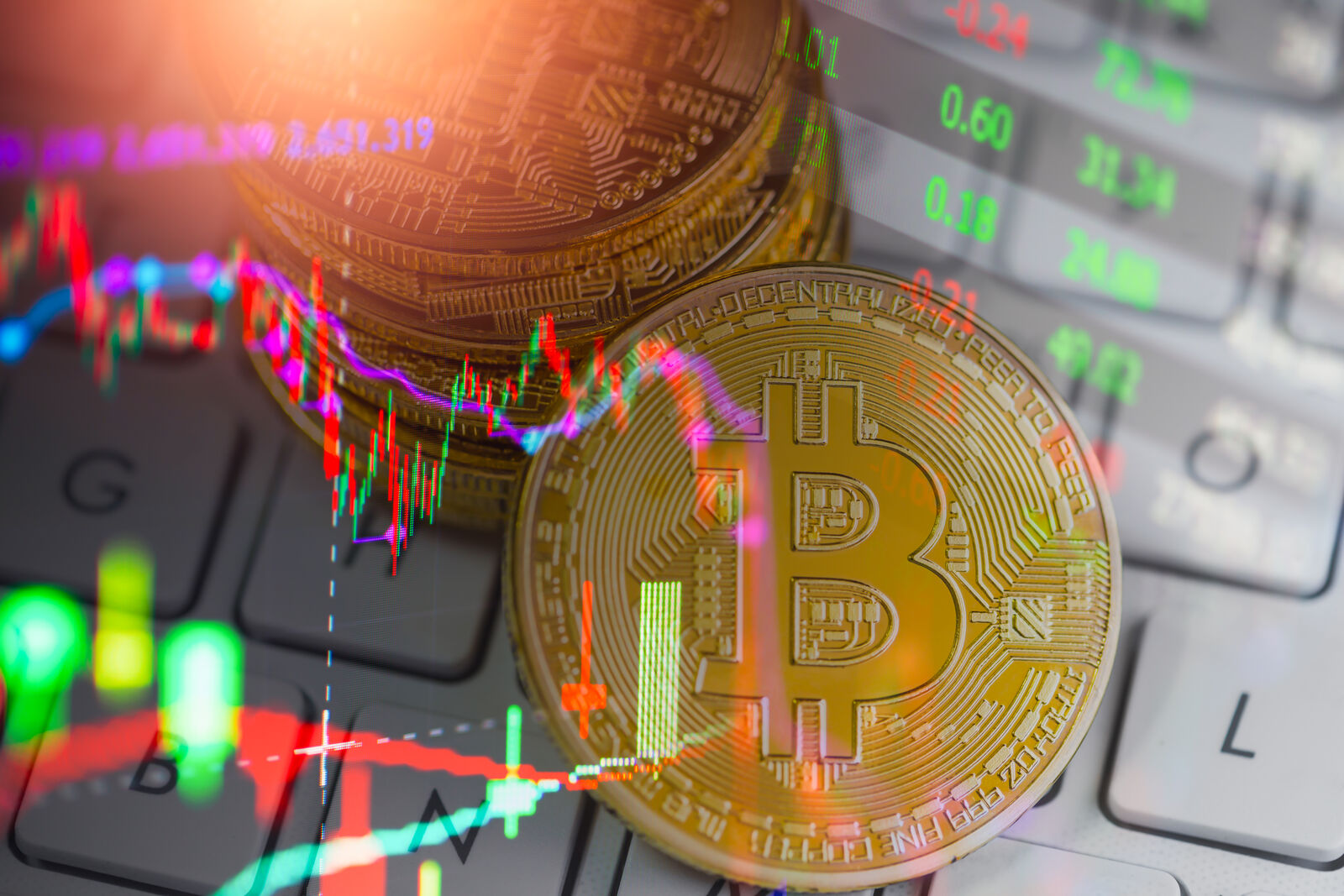 Zlatni bitkoin novčići na tastaturi laptopa preko kojih je prikazan grafikon kretanja vrednosti kriptovaluta